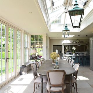 Conservatory with floor to ceiling glass windows and doors with white frames and large wooden dining room table and chairs
