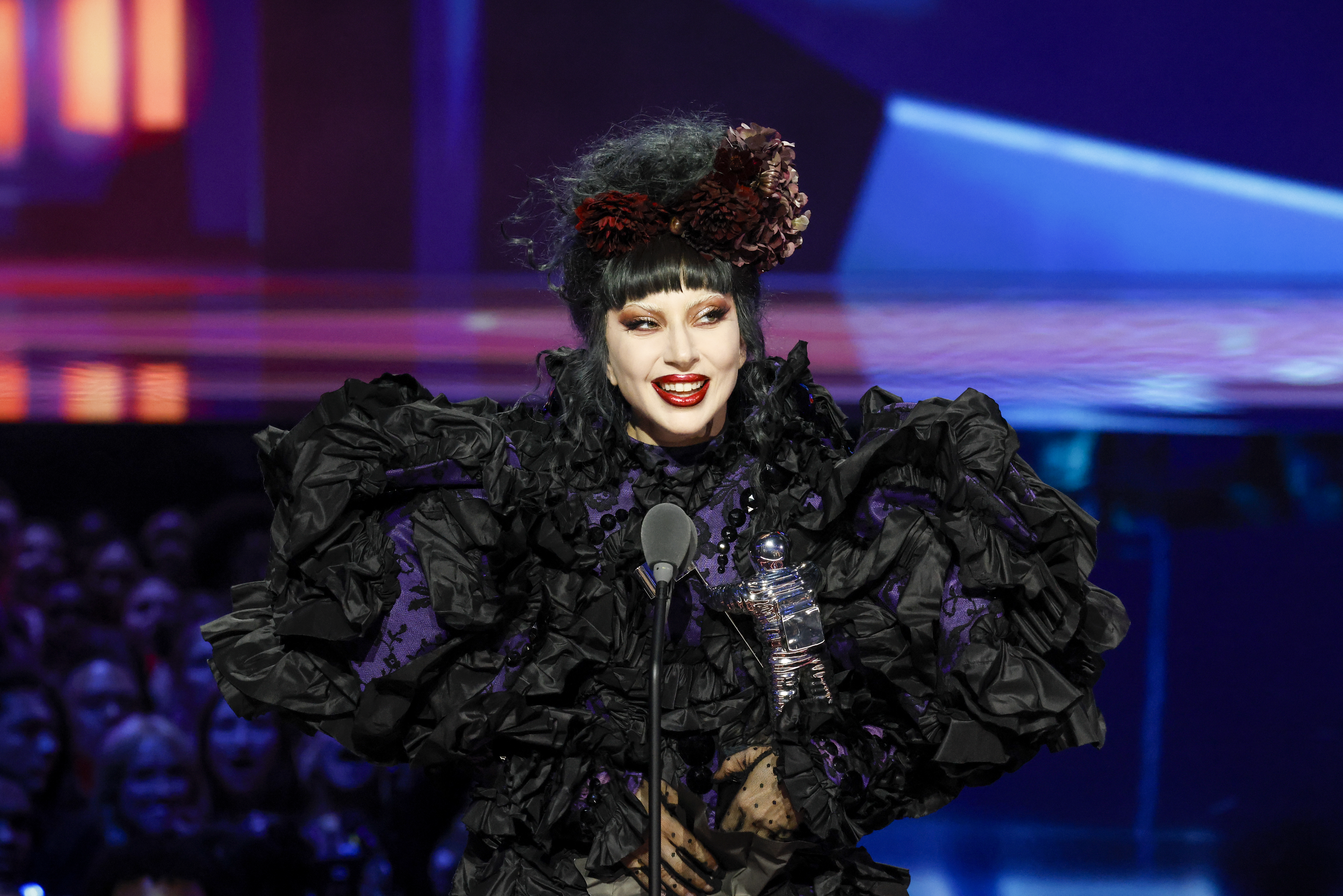 lady gaga on stage wearing an all black gown with her hair in an updo with flower attachments