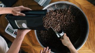 A large vat being filled with coffee beans by two people