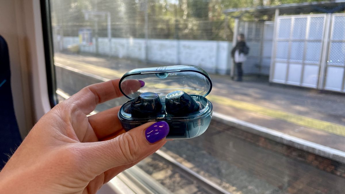 Sony WF-C710N earbuds in 'blue glass' on a grey table, with a woman's hand holding one of the earpieces