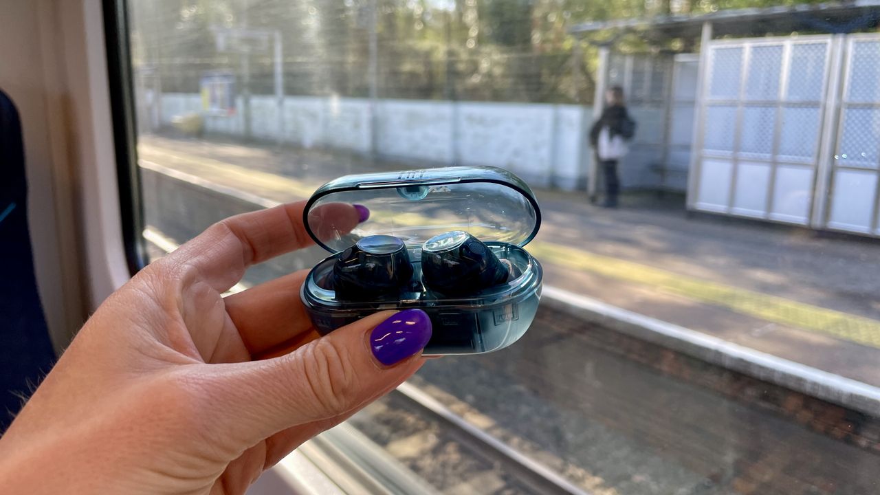 Sony WF-C710N earbuds in 'blue glass' on a grey table, with a woman's hand holding one of the earpieces