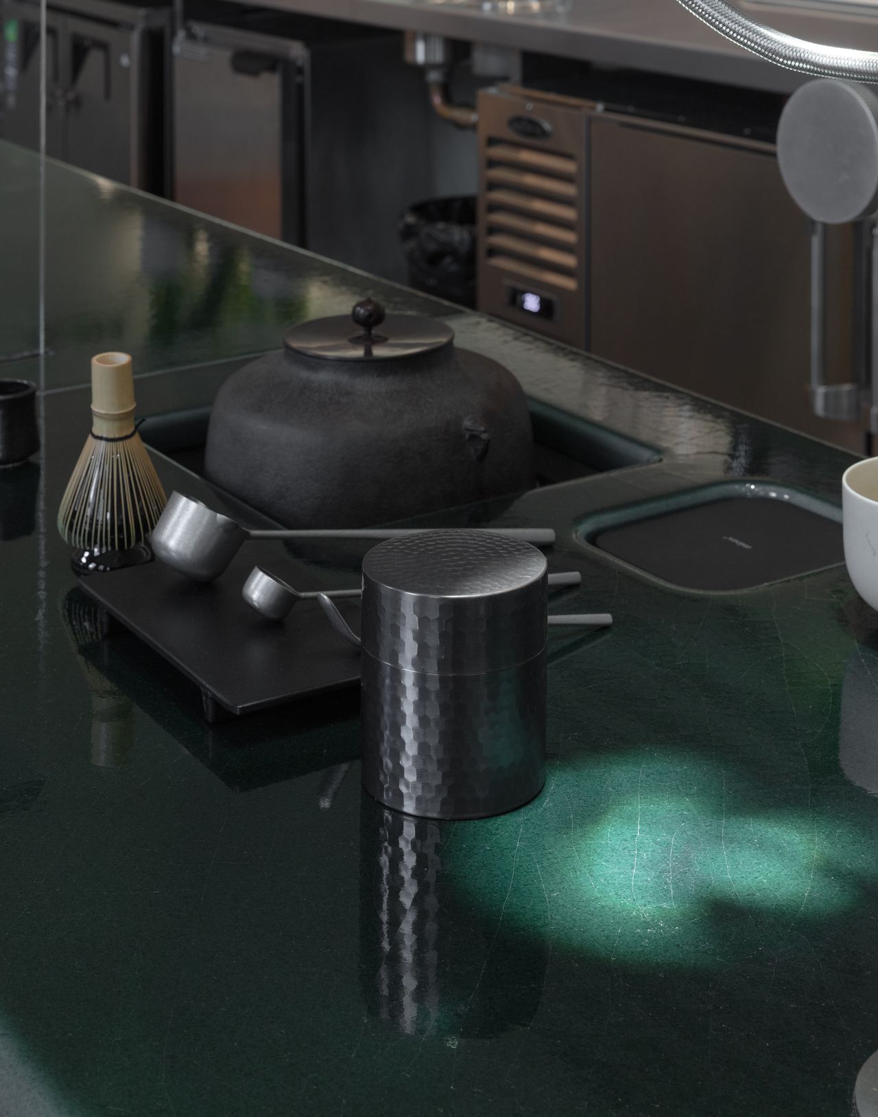A futuristic matcha cafe features Japandi interiors punctuated by wood, chrome, or emerald green tones, and a sci-fi-esque bar setup with dripping water bottles and lights.