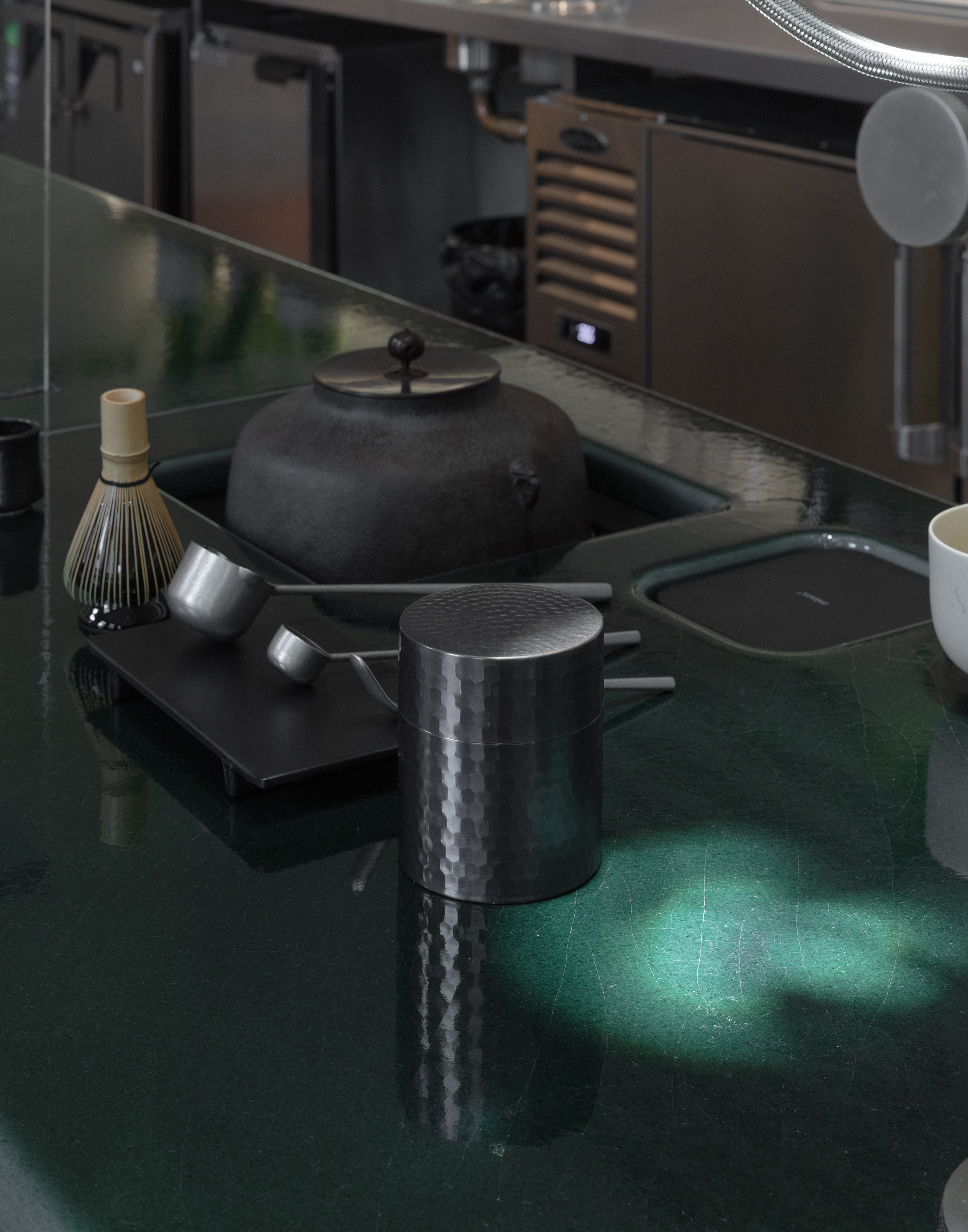 A futuristic matcha cafe features Japandi interiors punctuated by wood, chrome, or emerald green tones, and a sci-fi-esque bar setup with dripping water bottles and lights.
