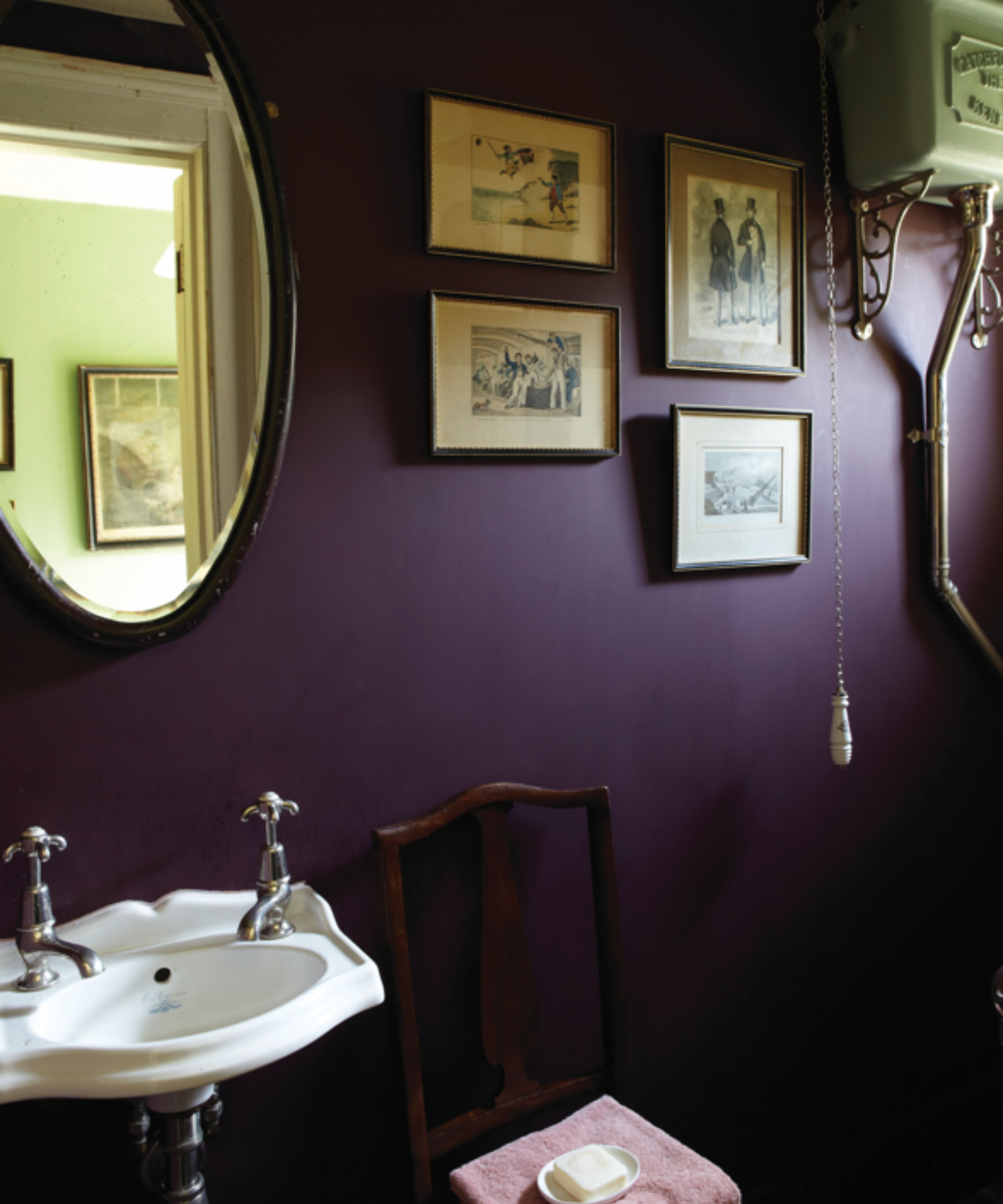 small powder room color drenched in a dark plum purple paint by farrow &amp;amp; ball with a small basin, antique chair, vintage artwork and a traditional high-level cistern toilet