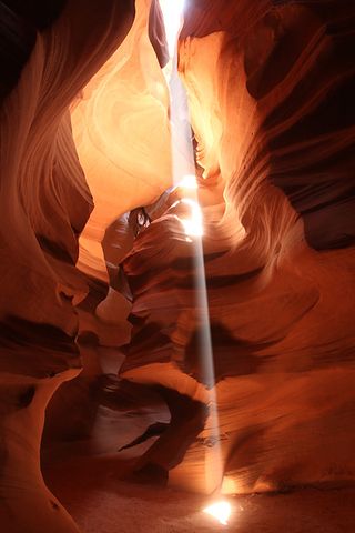 haft of sunlight penetrates Arizona's Upper Antelope Canyon through a gap in the walls, bathing the interior in a rich, warm glow of yellow, orange, and red