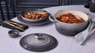 Beef bourguignon made in a grey Le Creuset dutch oven, placed on a white tablecloth with grey Le Creuset plates