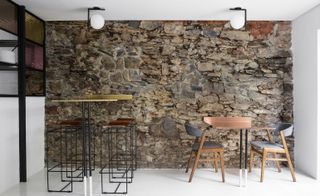 A high table with chairs and a square table with chairs next to the rustic wall