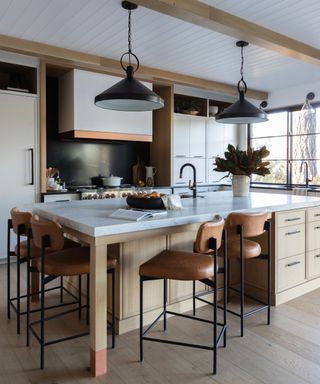 A wood kitchen island with a white countertop and brown leather bar stools