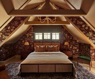 A log cabin bedroom with a dramatic pitched ceiling, wooden beams, floral wallpaper covering the walls, and a large double bed at the center