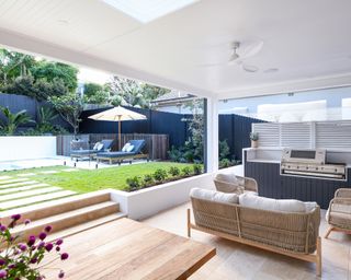 A covered seating area with a path leading up to an outdoor pool area in a small garden