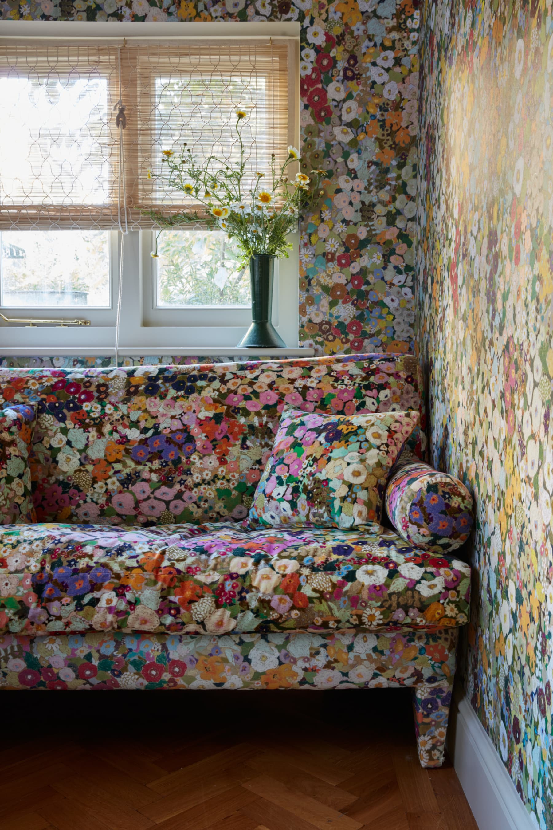 floral sofa with matching wallpaper, timber herringbone floors, and windows with bamboo blinds and a vase of flowers