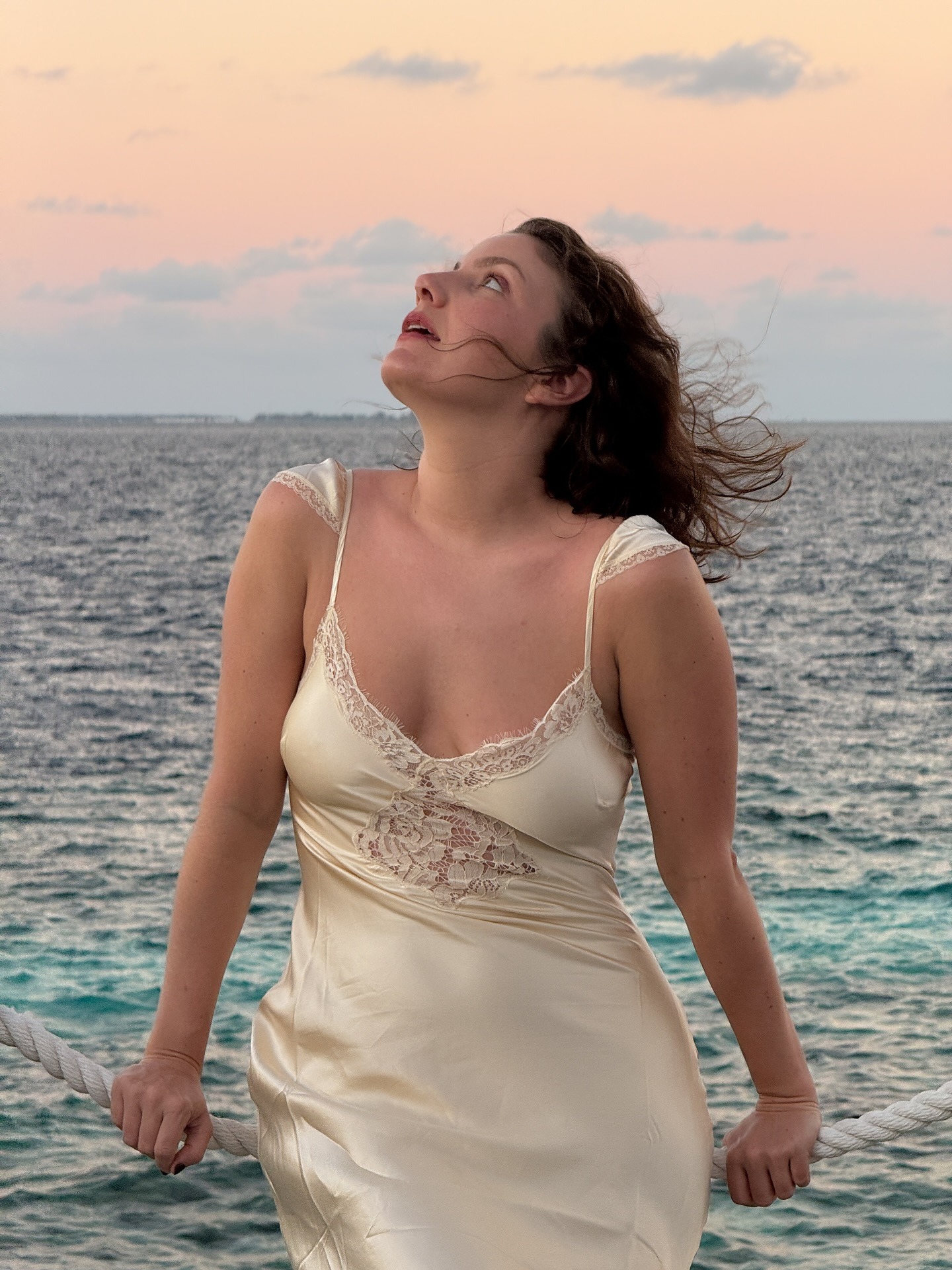 A woman staring out to sea in a cream silky dress