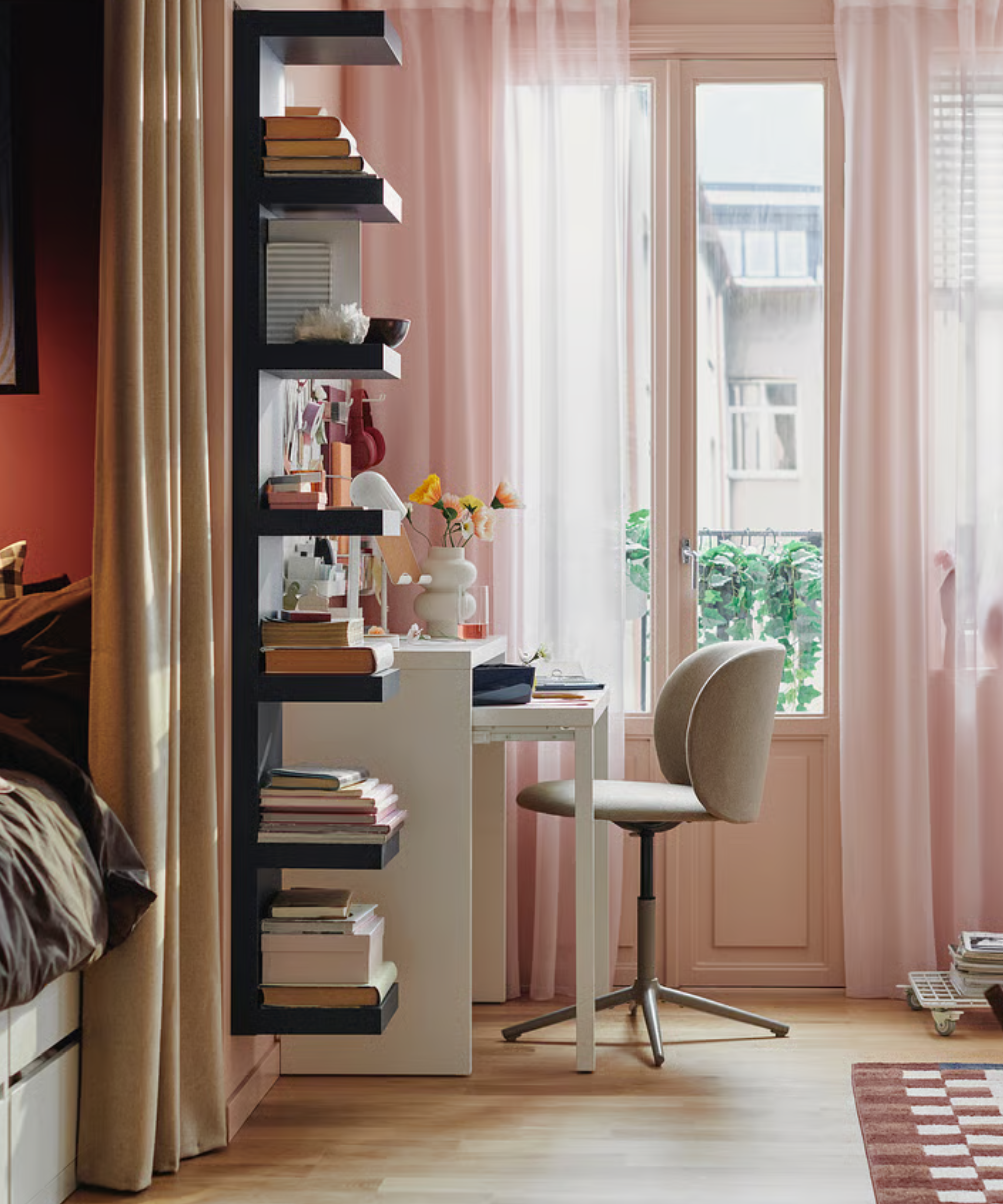 a bedroom with pink drapes in front of the windows, a black wall-mounted shelving unit, and a white pull-out desk