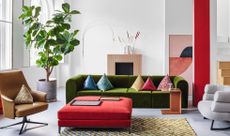 A living room with a green couch and red ottoman