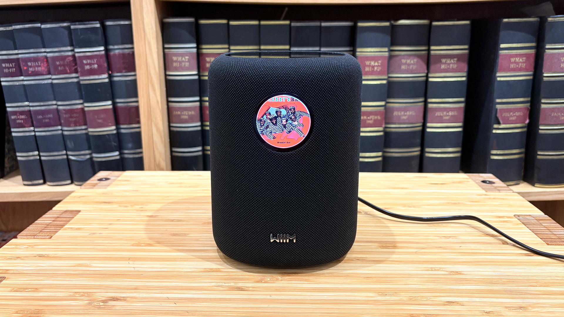 WiiM Sound wireless speaker in black on wooden hi-fi rack in front of bookcase