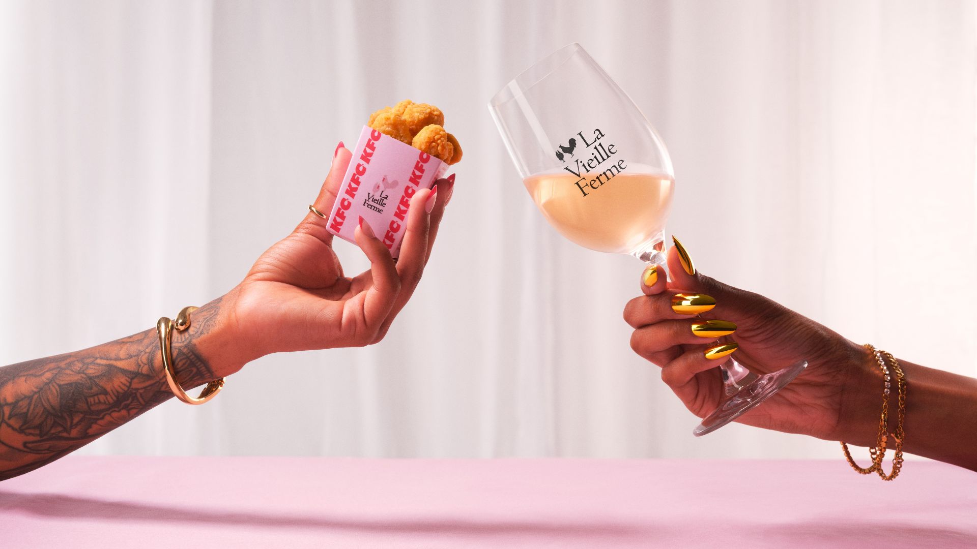an image of someone cheersing a small bucket of chicken against a La Veille Ferme branded wine glass with ros&eacute; in it