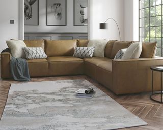 A tan leather sofa with grey rug, herringbone wood-effect LVT