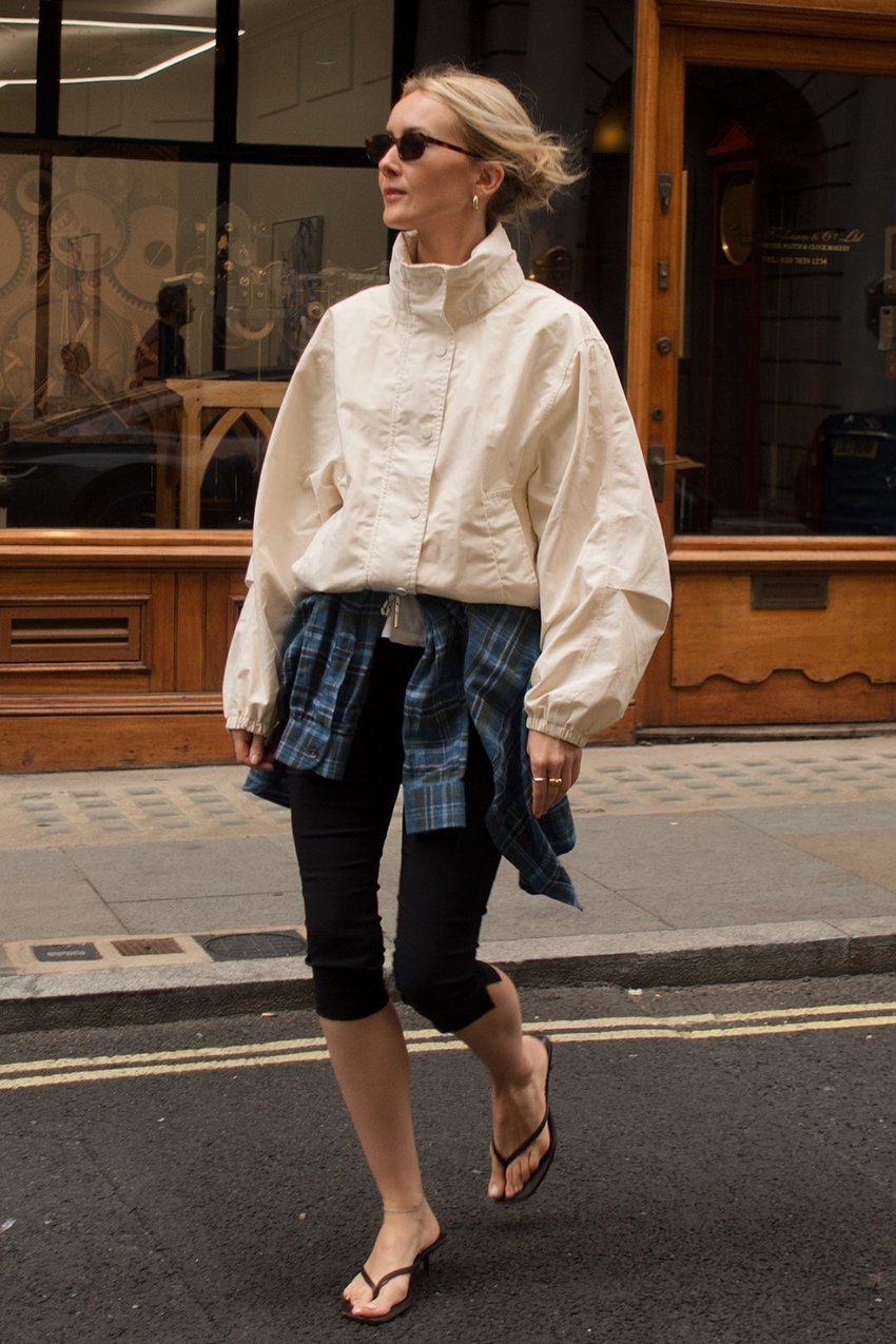 a woman wearing a white windbreaker, black capri leggings and black flip flops