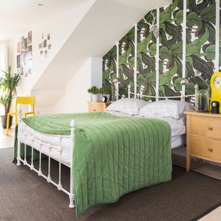 bedroom with botanical feature wall behind white wrought iron bedstead