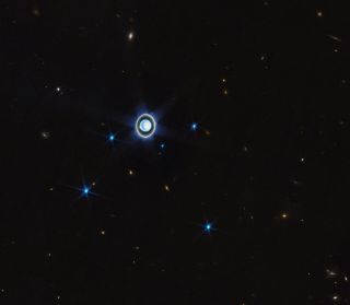 photo showing uranus as a bright blue dot against the blackness of space, with a distinct ring system around it.