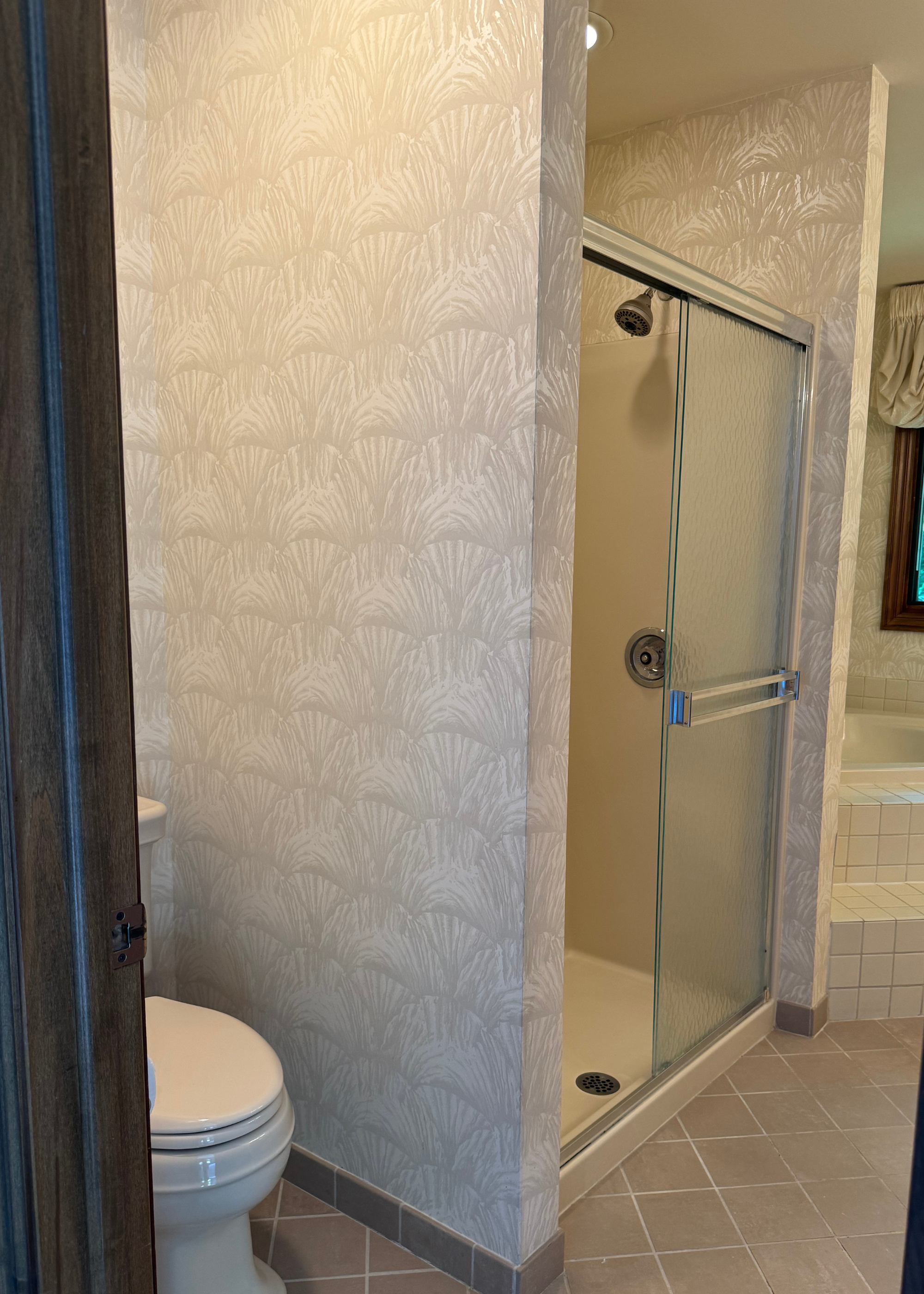 a wallpapered walk-in shower in a very outdated bathroom