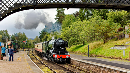 Flying Scotsman Steam Train at Boat of Garten Scotland with people on the platform as the train enters the station