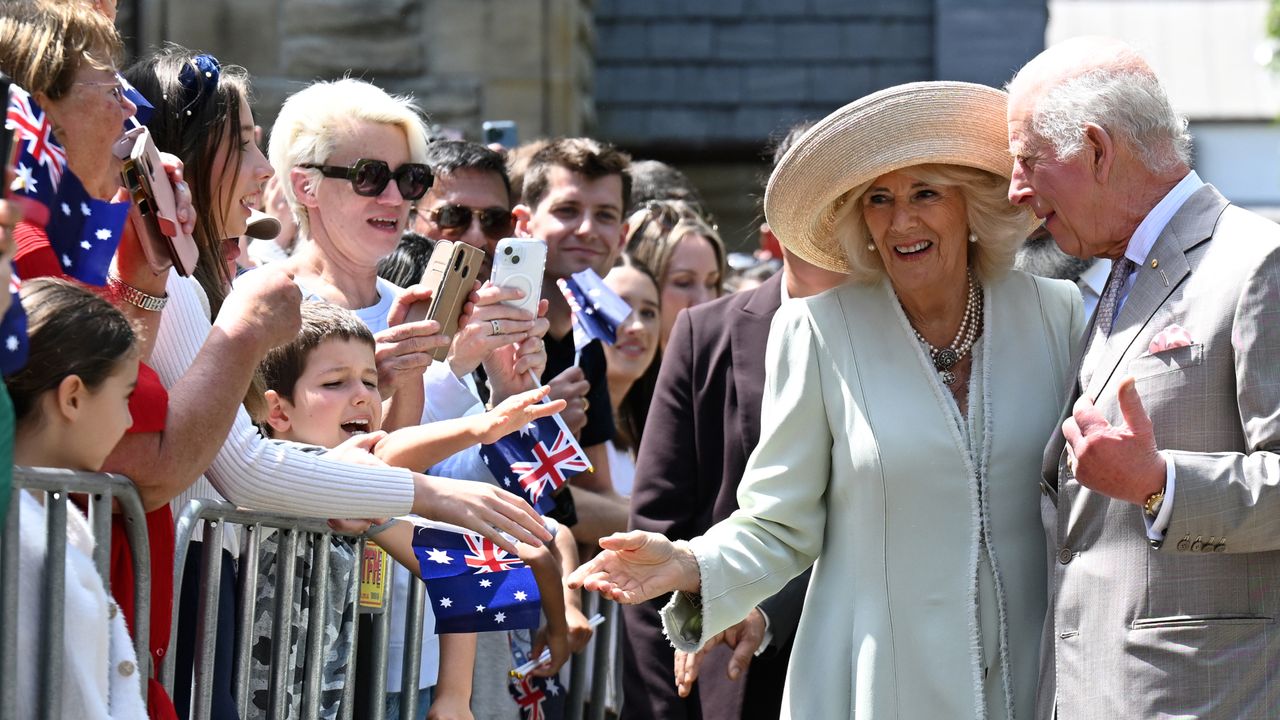 King Charles and Queen Camilla smiling and greeting a crowd of Australian fans outside a church