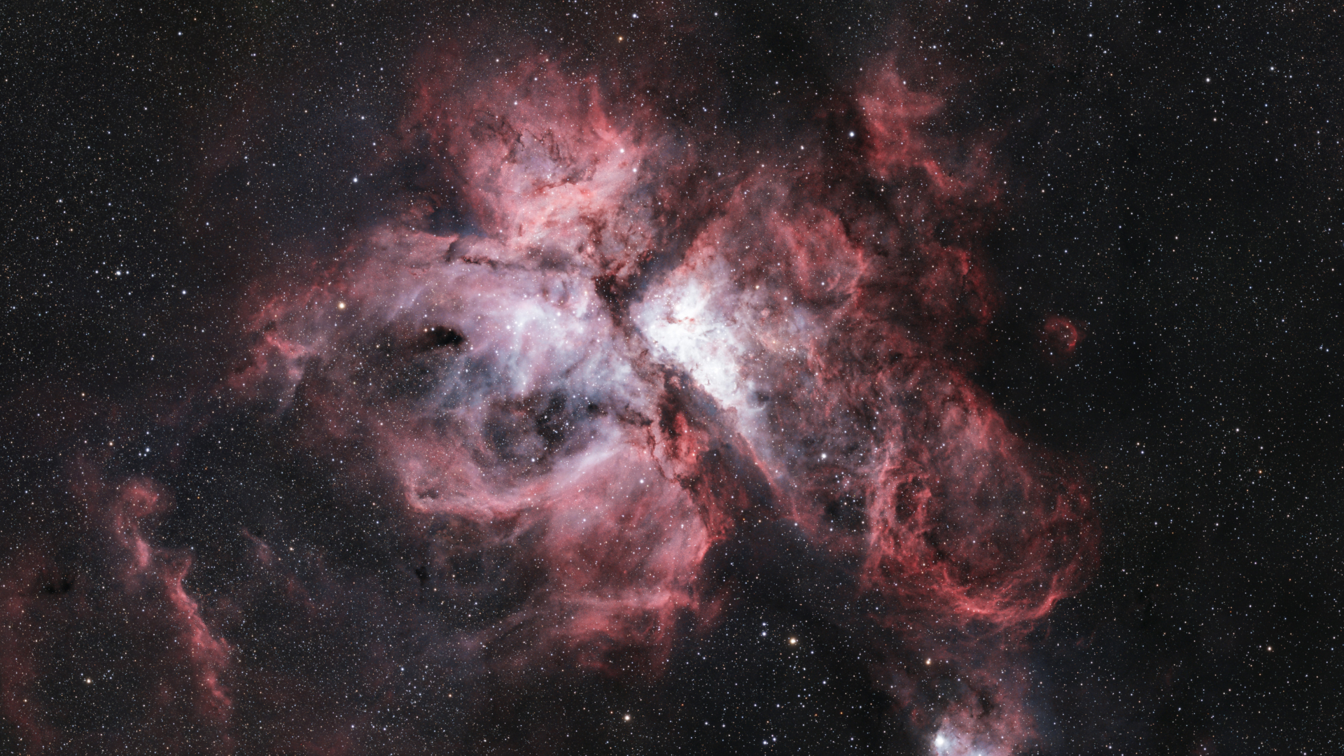 The reddish swirling clouds of the Carina Nebula are pictured against a distant starfield on a dark sky. Its central region glows brightly and is intersected by dense dusty filaments.