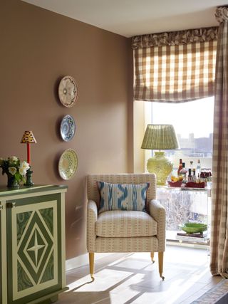 Living room painted in ochre with patterned armchair and gingham blinds.