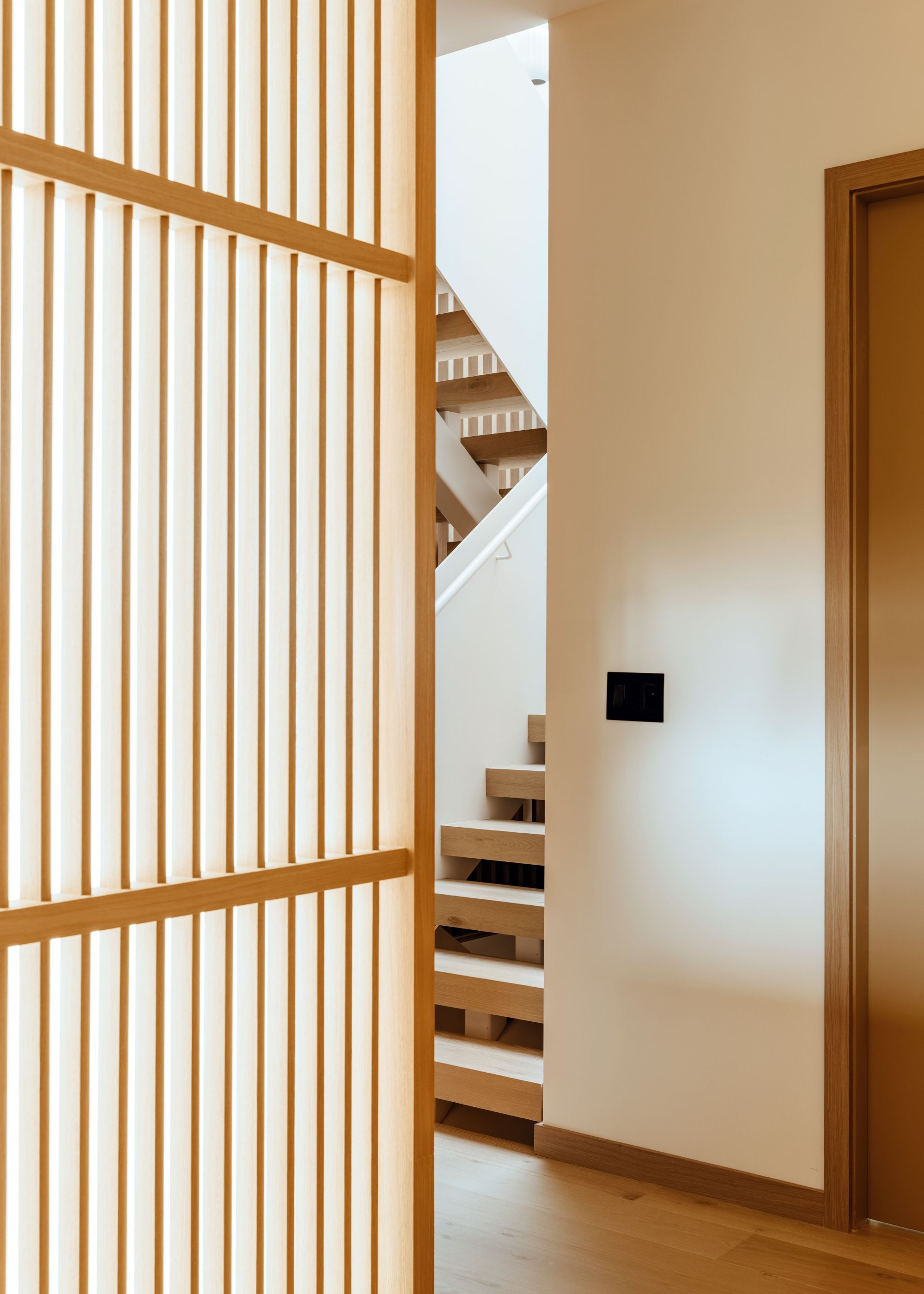 A wooden screen, a staircase, and a switchboard in a white room