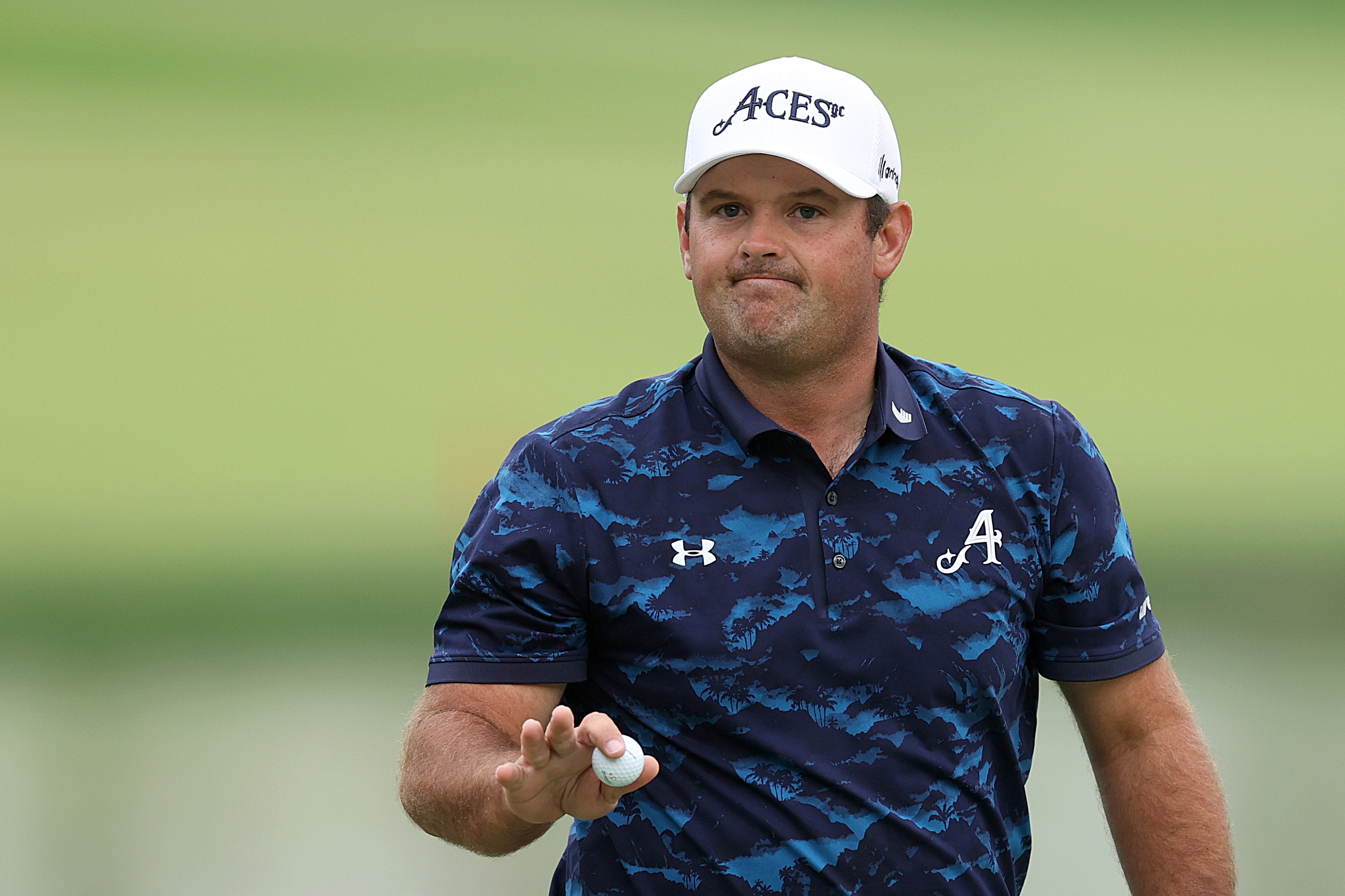 Patrick Reed waves to the crowd holding a golf ball
