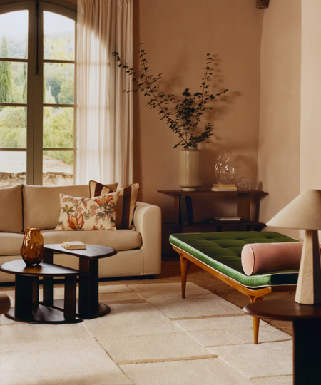 a living room with a couch, a chaise lounge, a tan rug, and nesting tables