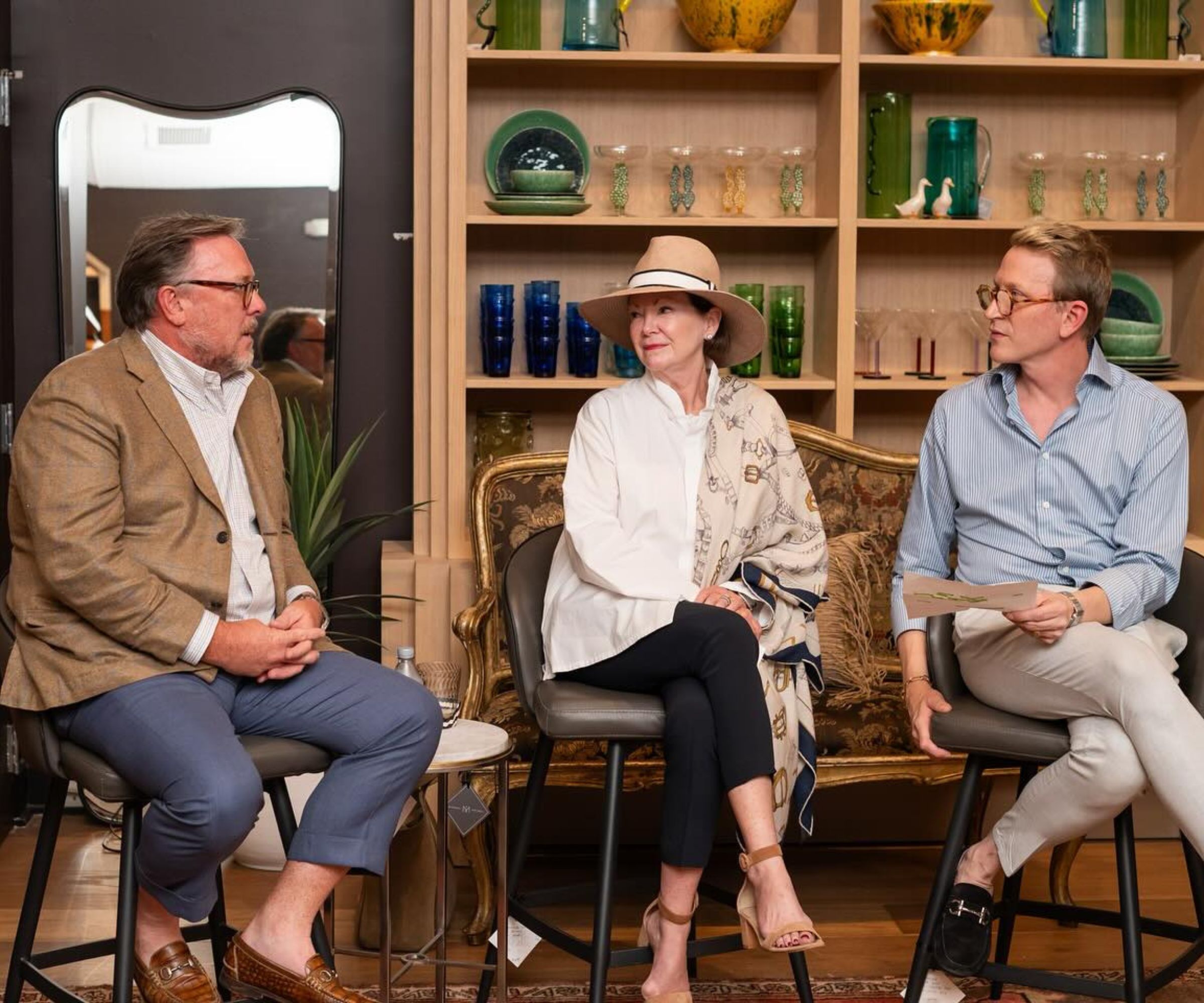 Three people sat on stools in a panel talk, shelving decorated with glassware behind them