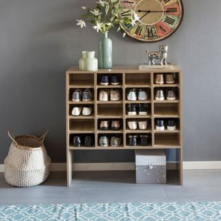 Grey walled hallway with a cubbyhole storage cabinet with flowers and a clock and a basket as décor