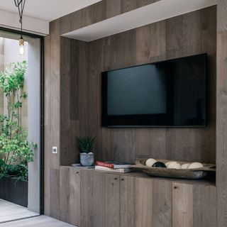 A TV unit in a living room covered in dark wood vertical slats