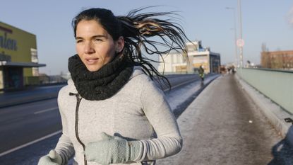 Woman running wearing thick jumper, gaiter and gloves
