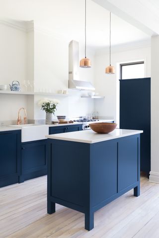 A white kitchen with navy blue kitchen cabinets and island, white countertops and pale wooden flooring.