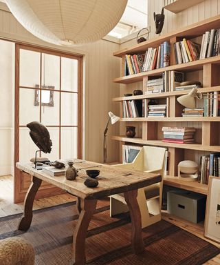 Neutral study with floor to ceiling bookshelf, round lantern pendant, wooden desk, floor lamps