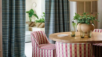 a dining room with striped chairs and curtains, with glasses and a vase on the table