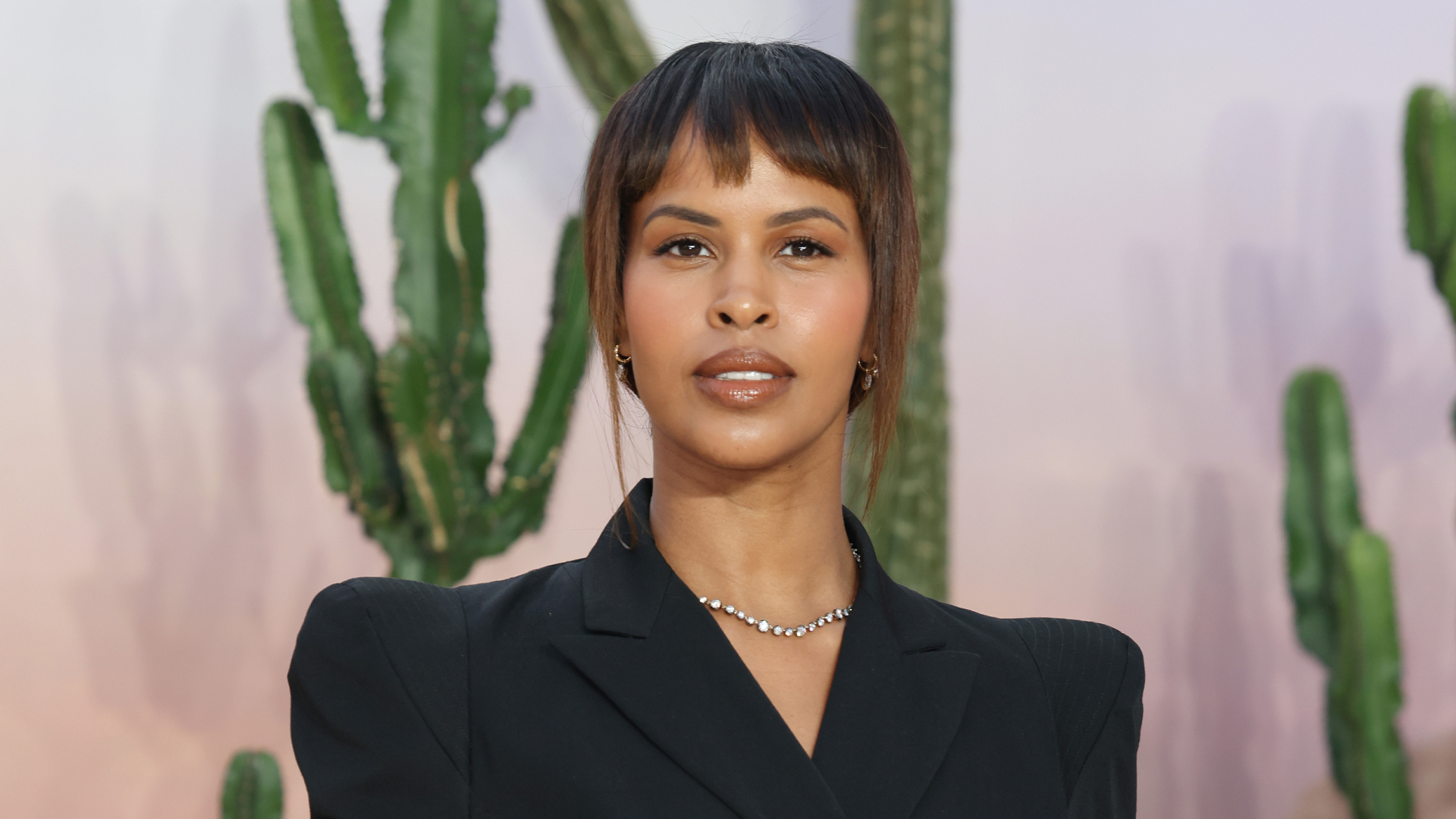 Sabrina Elba wearing a black blazer with shoulder pads and a ponytail hairstyle. 