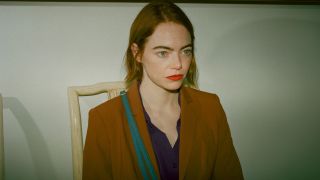 Emma Stone in Kinds of Kindness wearing an orange blazer and purple shirt and looking straight forward.