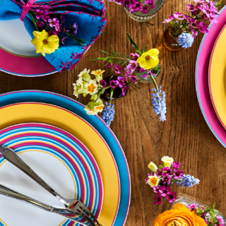 Wooden table with blue yellow and pink plates and flowers