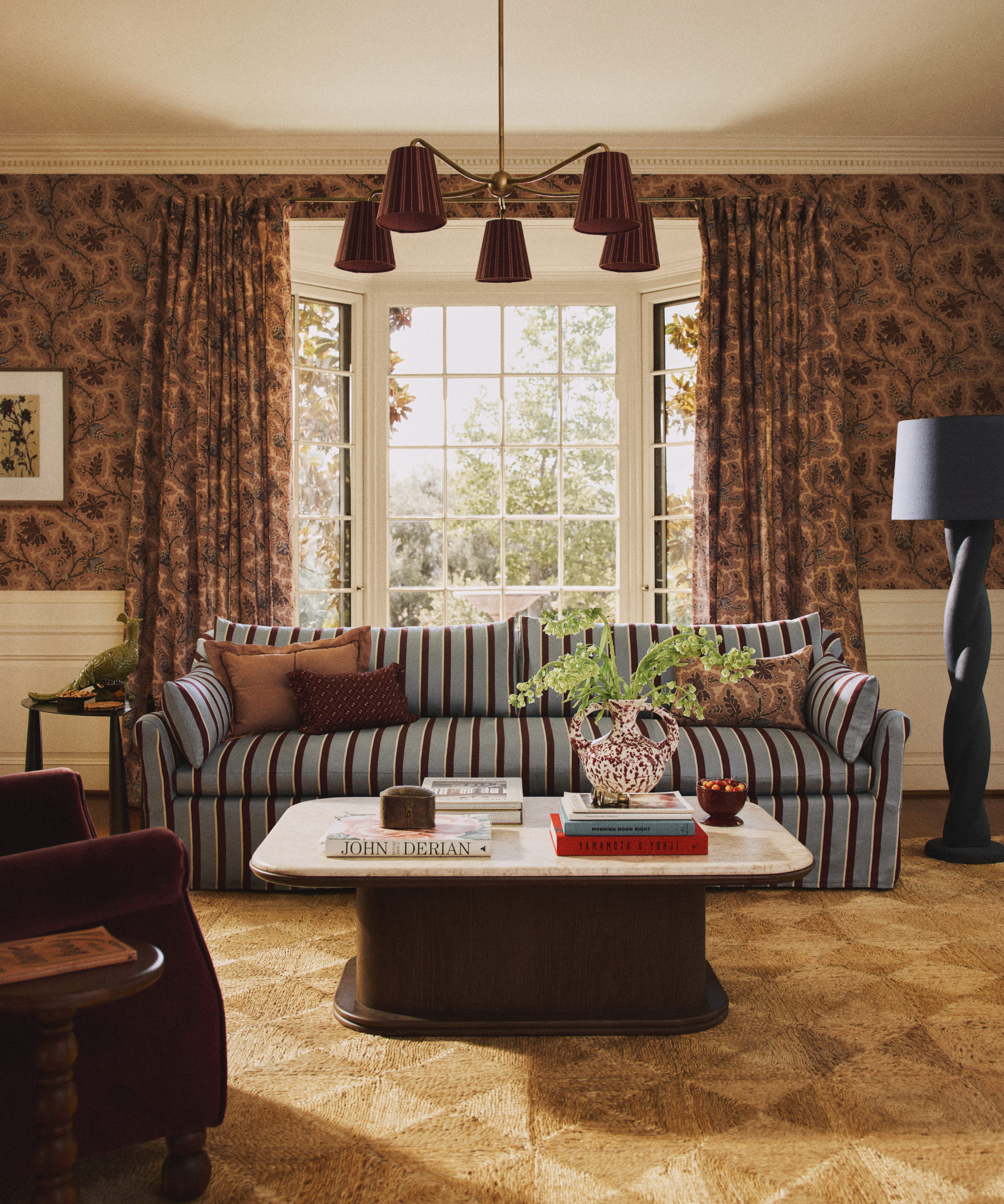 a living room with floral wallpaper, a blue and maroon striped couch, a woven rug, and a large coffee table