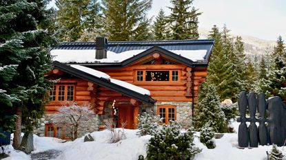 exterior of log cabin in snow with fir trees