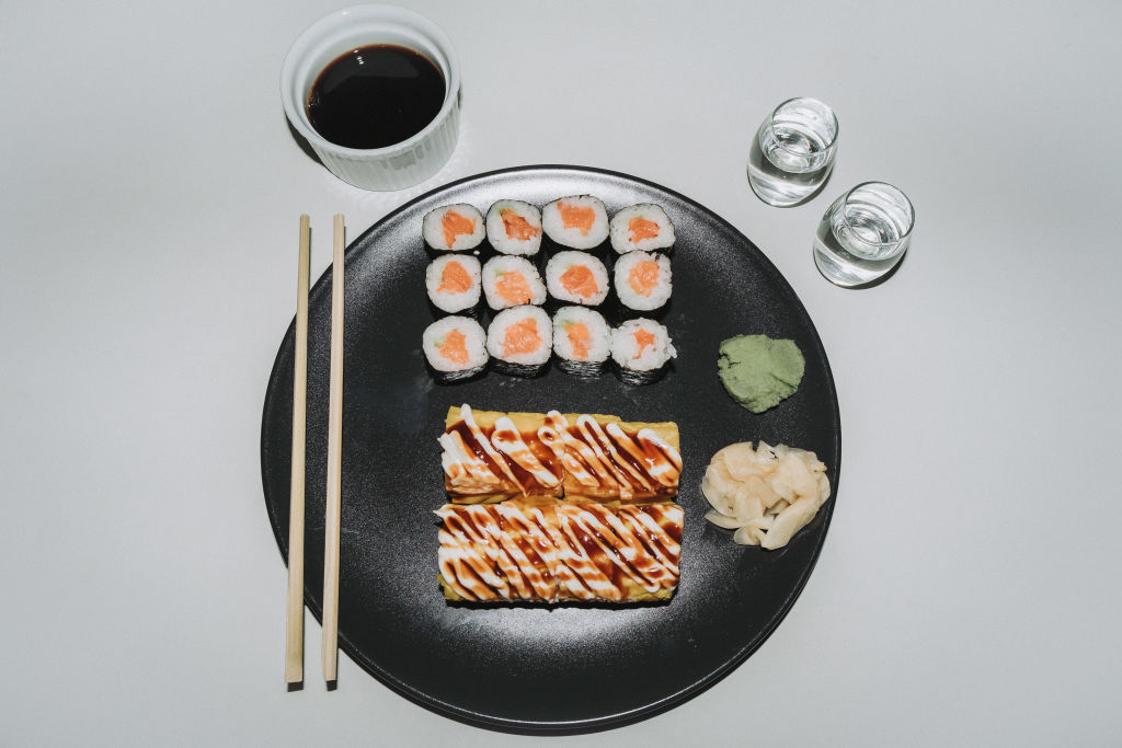 Banana sushi rolls and salmon maki sushi rolls are sitting on a plate next to two glasses of sake.