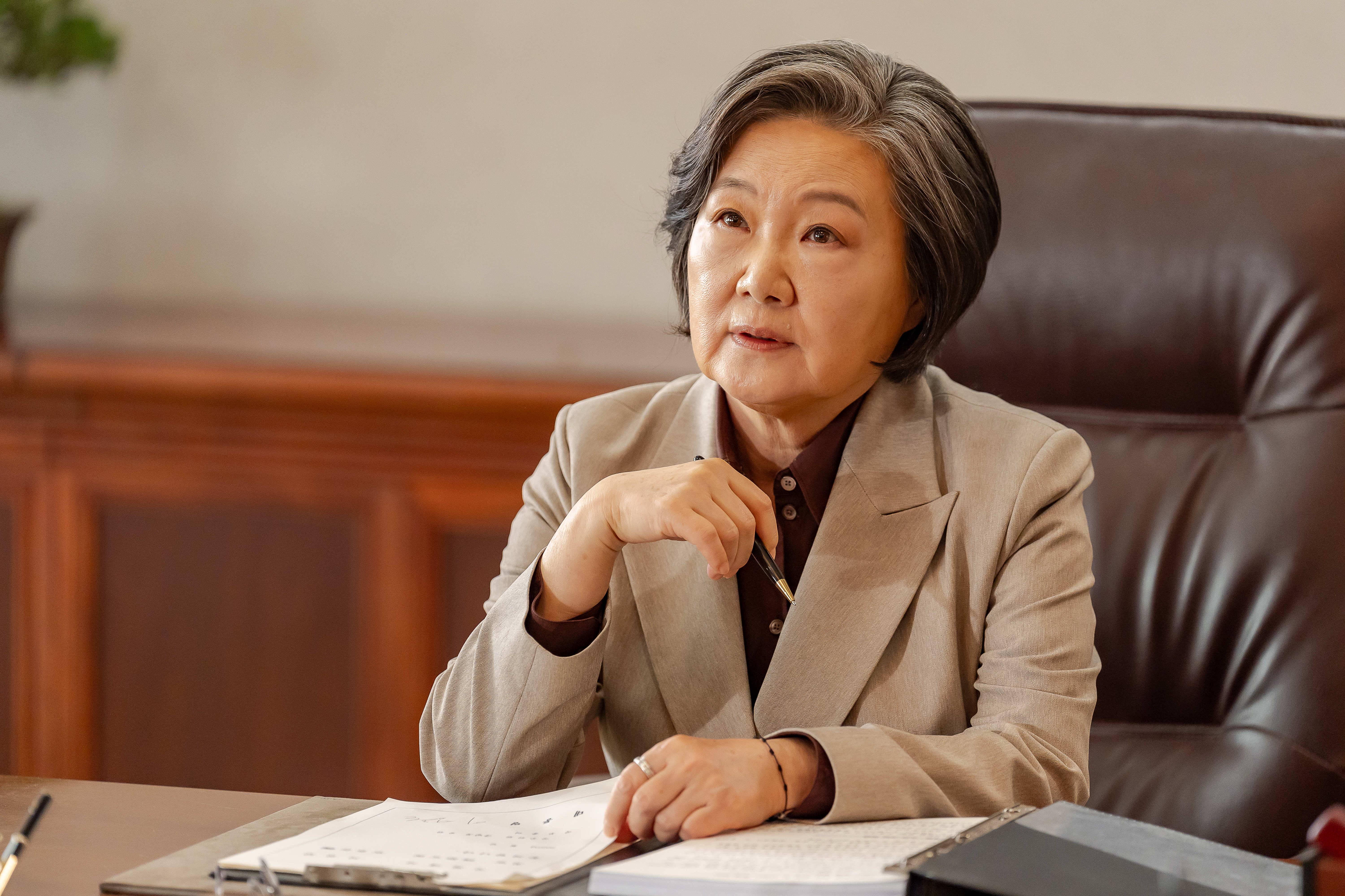 Kim Hae-sook wears a tan stui and sits at a desk in &#039;Tempest.&#039;