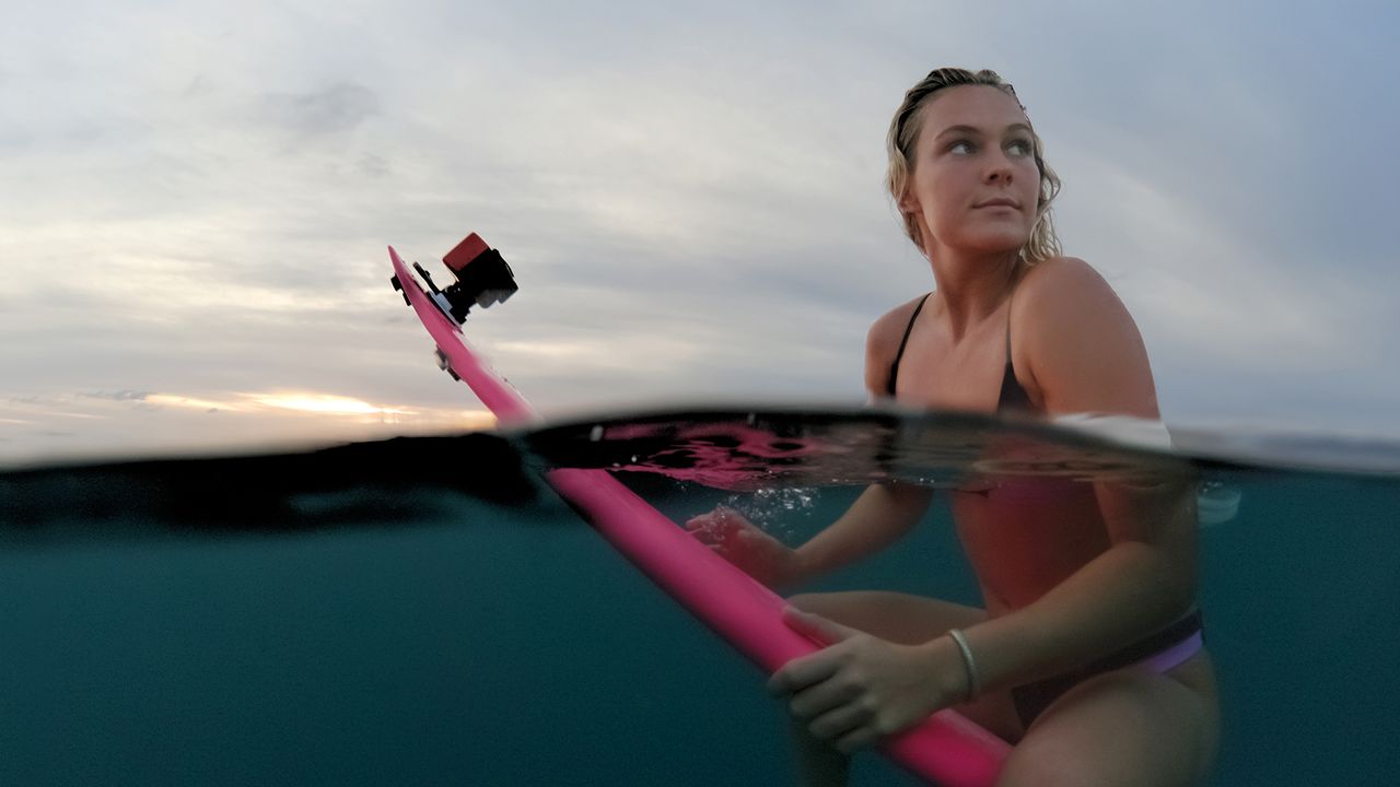 Female surfer sitting on a surfboard half underwater