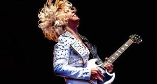 Samantha Fish leans back as she takes a solo on her white Gibson SG. She wears a white studded jacket.