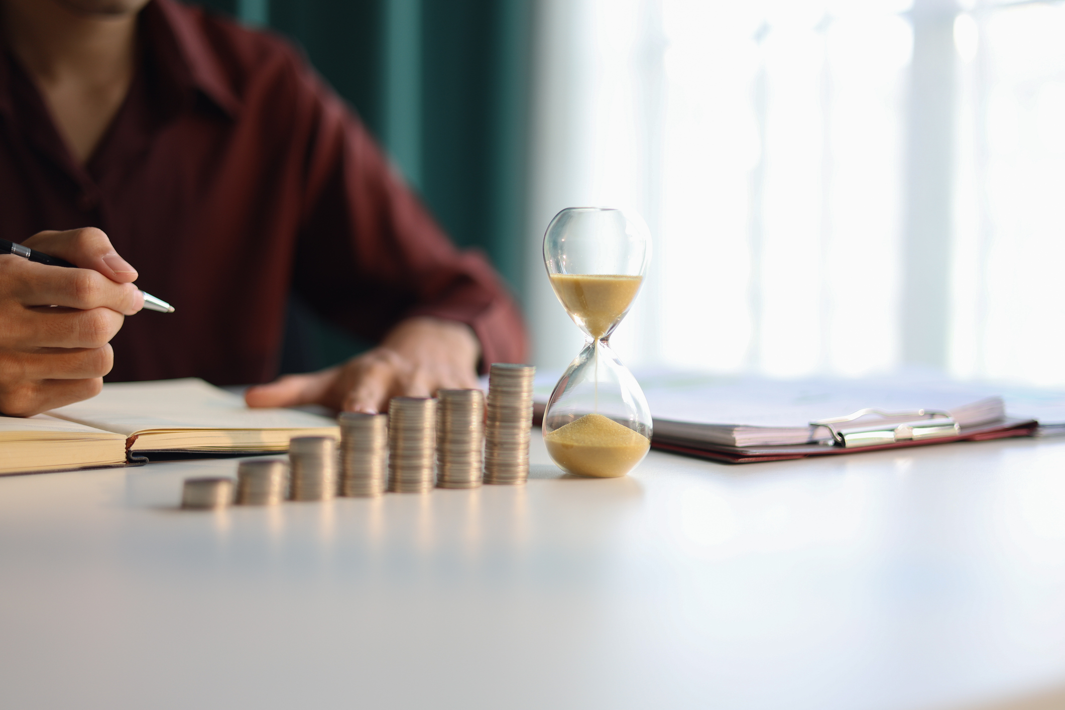 Rising stack of coins and running sand clock on the table. Growing of income, saving or return investment through time representing 'boring' traditional defensive stocks