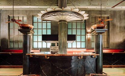 A view of the open kitchen in the center of the restaurant, built in industrial architecture style, with copper-toned countertops and other details, while the rest is in black metal.